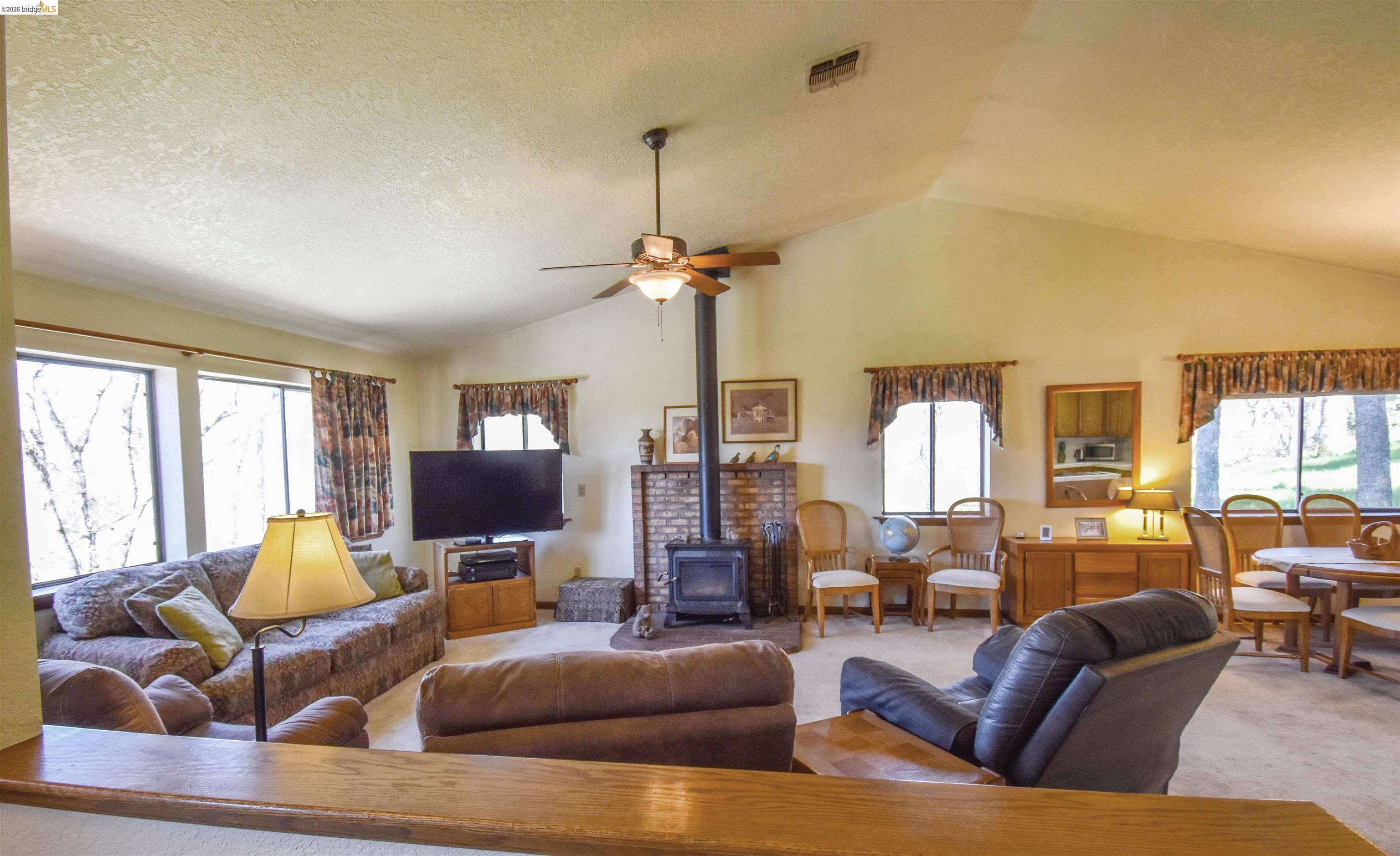 15170 Potato Ranch Road Sonora, CA 95370 - Photo 6 of 49 Living room featuring a wood stove, carpet flooring, ceiling fan, plenty of natural light, and a high ceiling