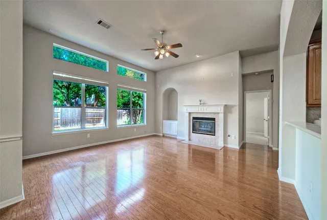 a view of an empty room with window wooden floor and a kitchen view
