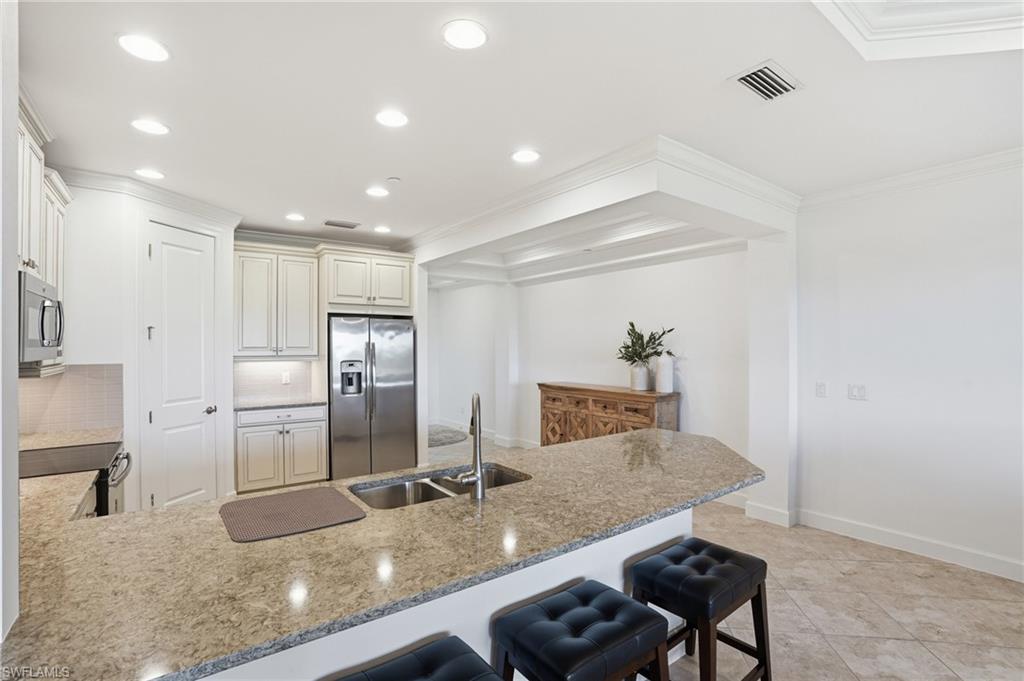 8773 Bellano Court, Unit 103 Naples, FL 34119 - Photo 18 of 47 Kitchen with a peninsula, a breakfast bar area, stainless steel appliances, light stone counters, and ornamental molding