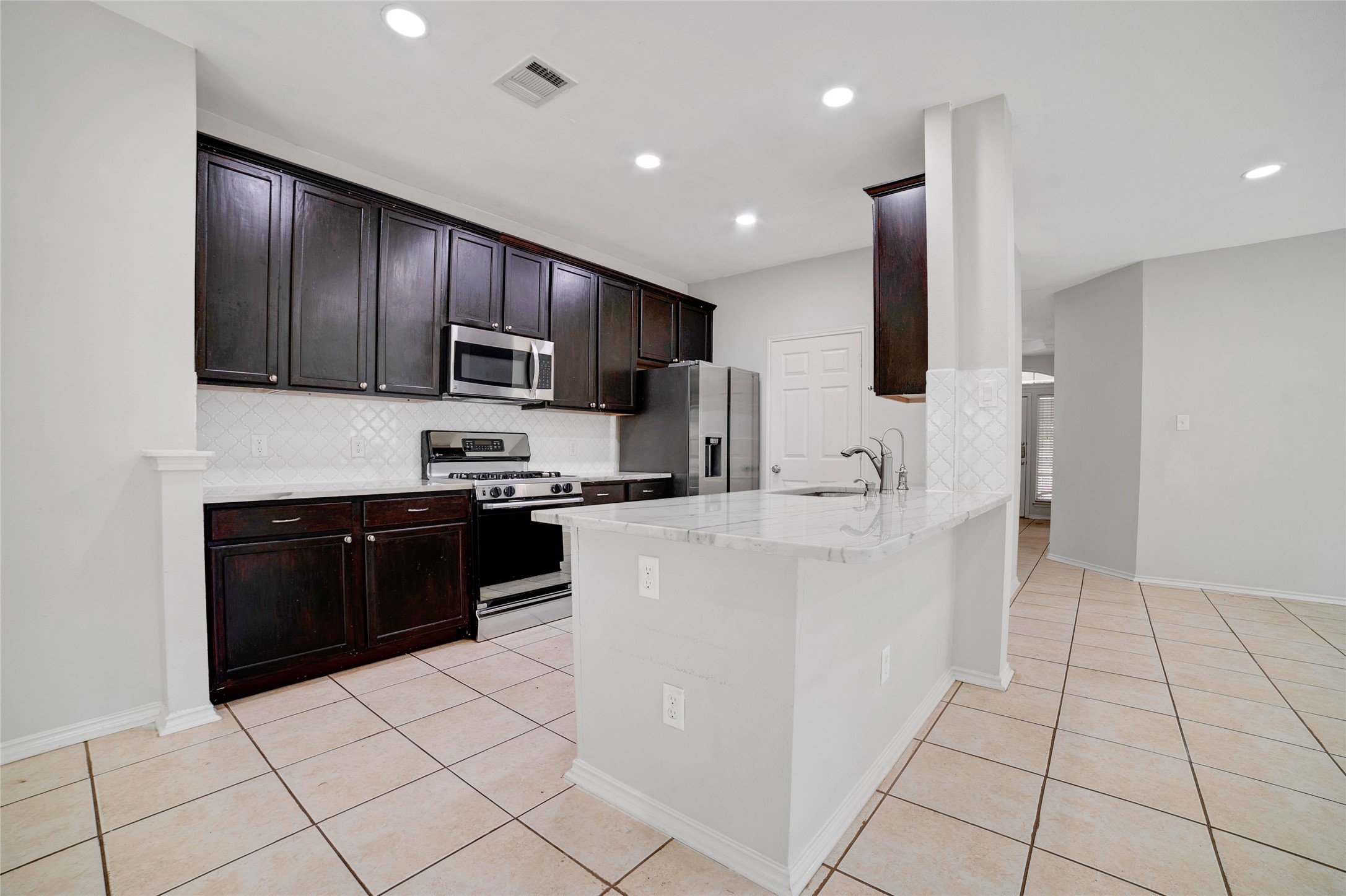 3630 Spring Canyon Trail Round Rock, TX 78681 - Photo 3 of 23 Kitchen with stainless steel appliances, dark wood finish cabinets, a peninsula, light stone countertops, and recessed lighting