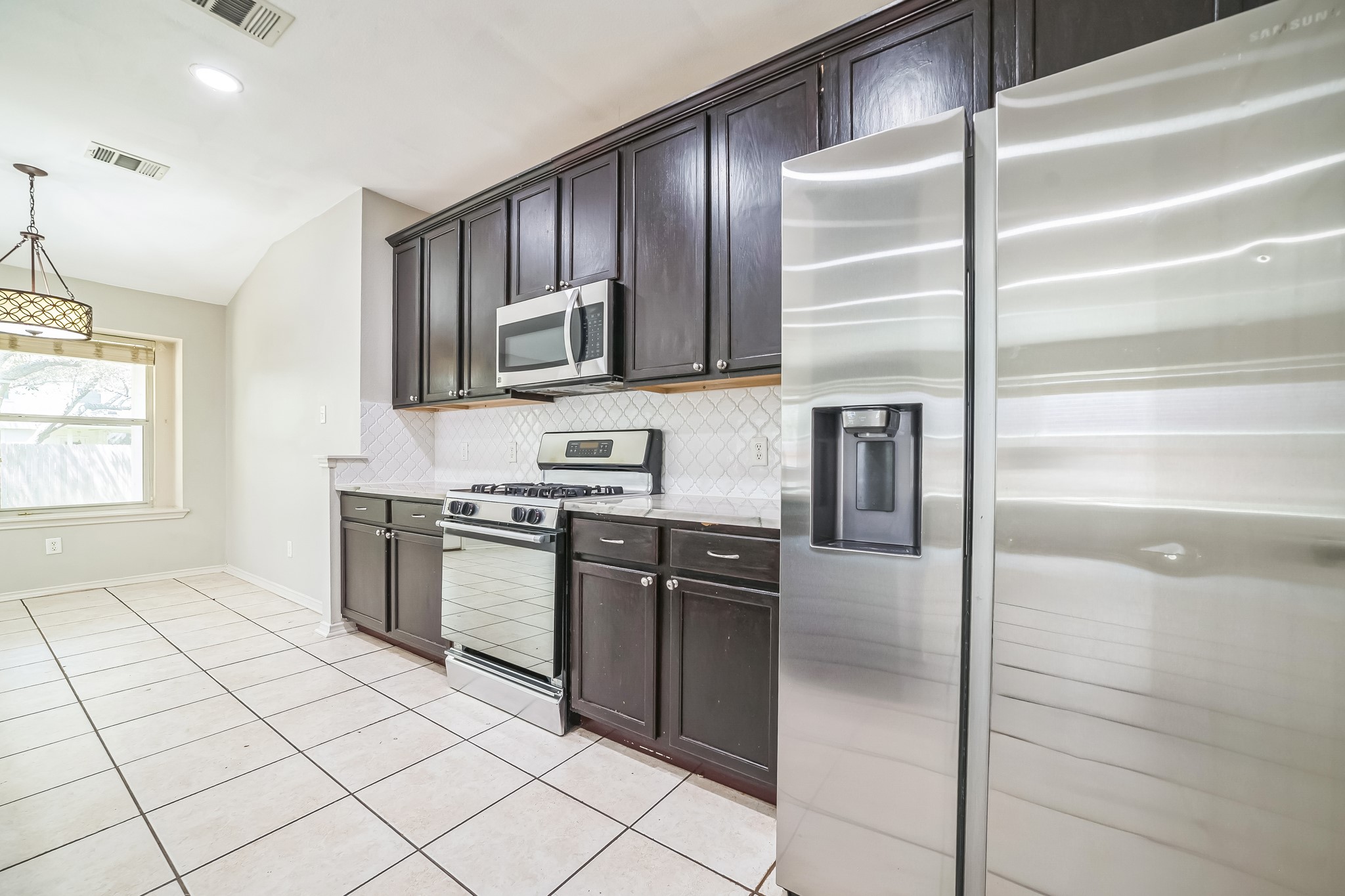 3630 Spring Canyon Trail Round Rock, TX 78681 - Photo 4 of 23 Kitchen featuring stainless steel appliances, lofted ceiling, dark wood finish cabinets, light tile patterned floors, and light stone counters