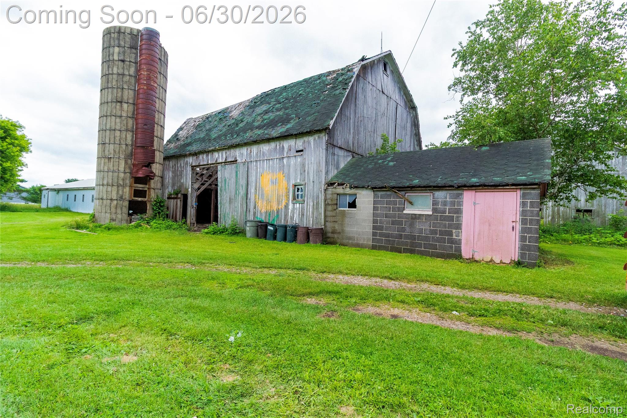 8150 Norman Road Imlay City, MI 48444 - Photo 7 of 58 Barn structure with vertical wood siding and a green shingle roof, accompanied by a concrete silo and a cinder block outbuilding