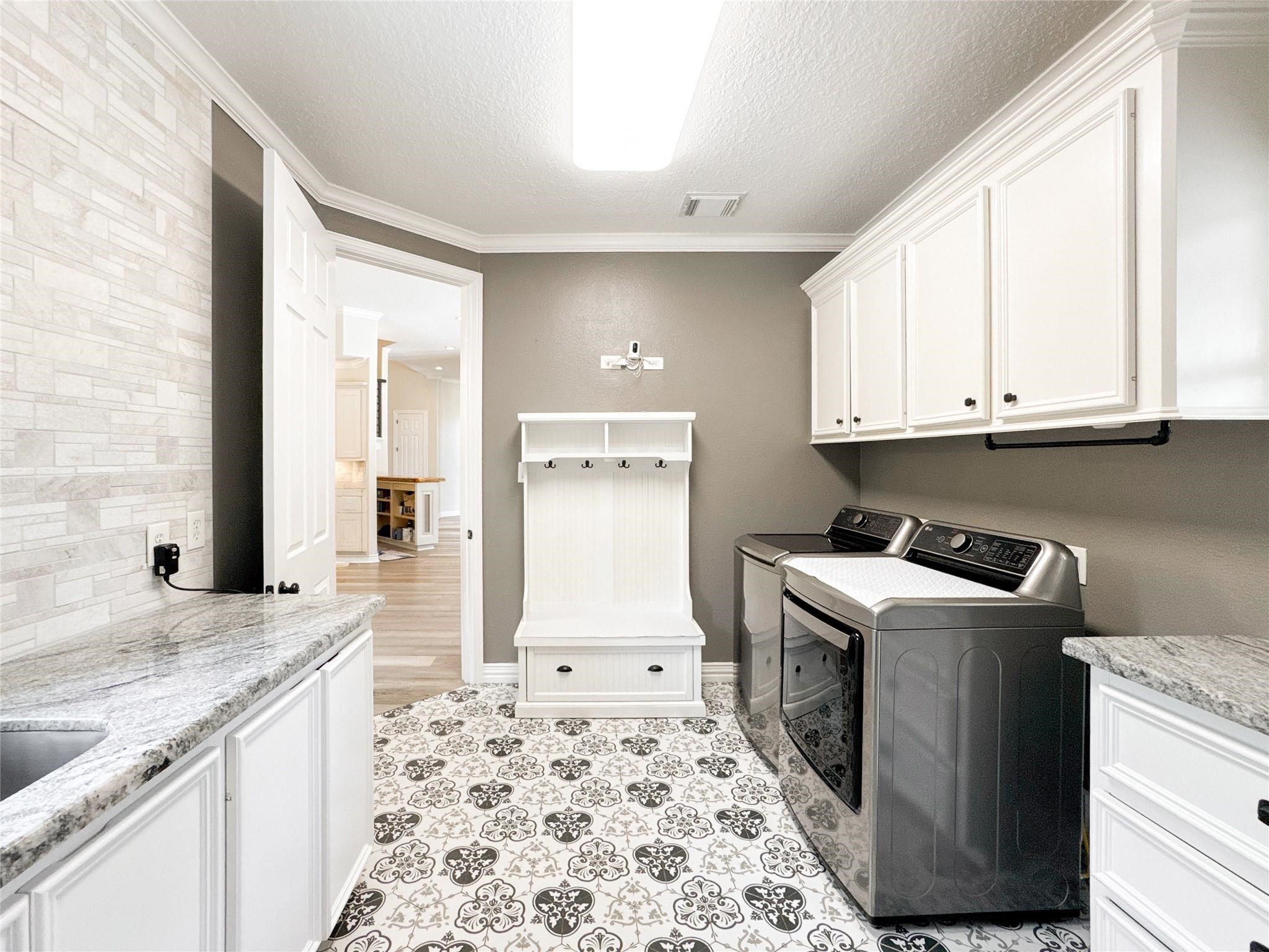 1810 Woerner Road Houston, TX 77090 - Photo 25 of 39 This photo showcases a bright, stylish laundry room with modern appliances, white cabinetry, and a patterned tile floor. The space includes ample storage and a convenient bench with hooks, perfect for organizing and managing household tasks.