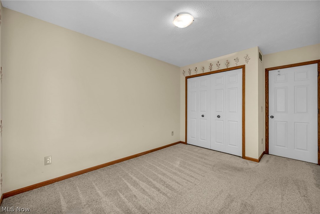 9842 Johnnycake Ridge Road Mentor, OH 44060 - Photo 19 of 40 Carpeted room featuring a ceiling-mounted light fixture, neutral wall paint, bi-fold closet doors, a separate paneled door, and wood-finish trim