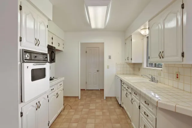a large white kitchen with granite countertop a sink and dishwasher a stove with wooden floor