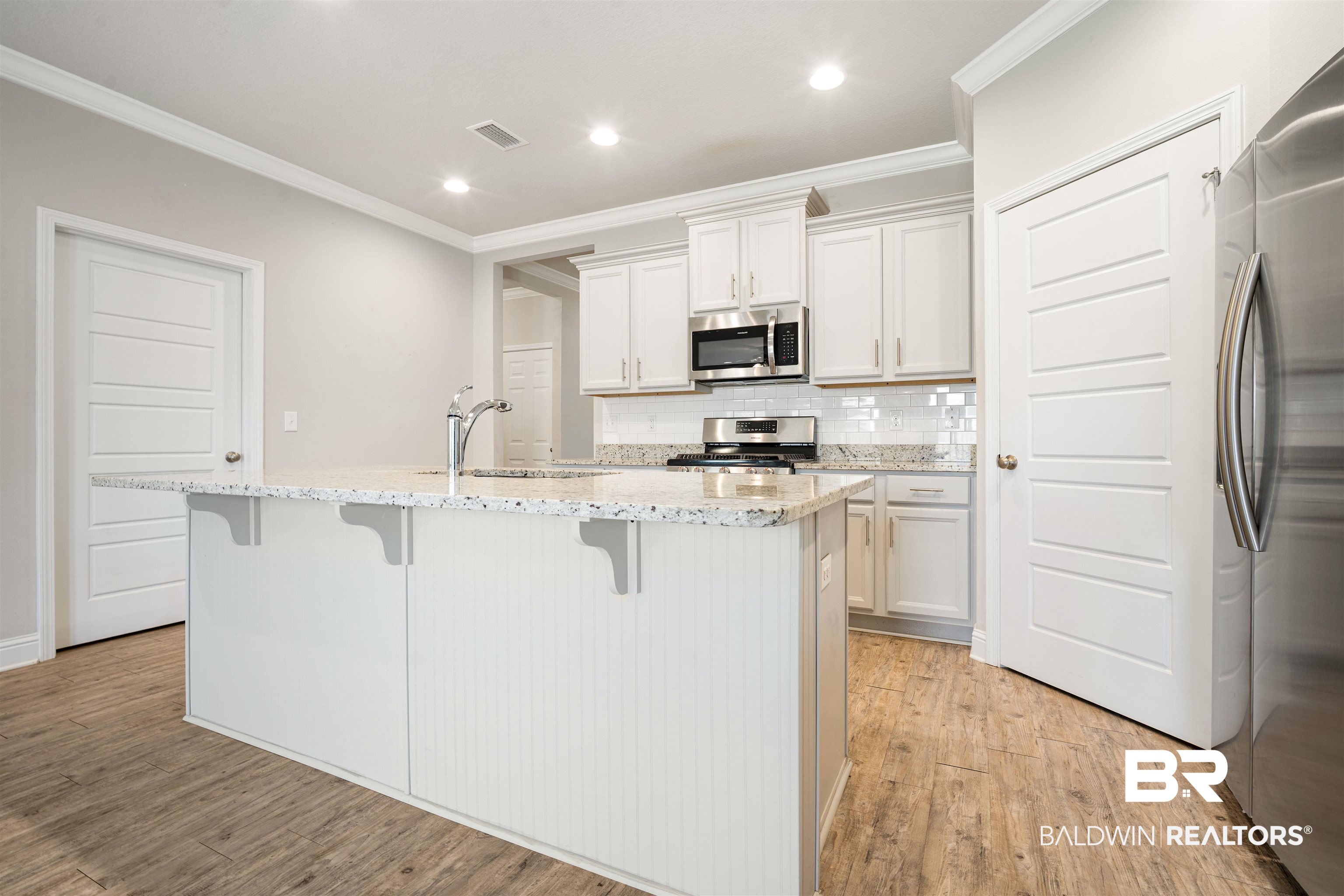 24479 Kipling Court Daphne, AL 36526 - Photo 8 of 41 Kitchen featuring decorative backsplash, light stone countertops, stainless steel appliances, crown molding, and a kitchen breakfast bar