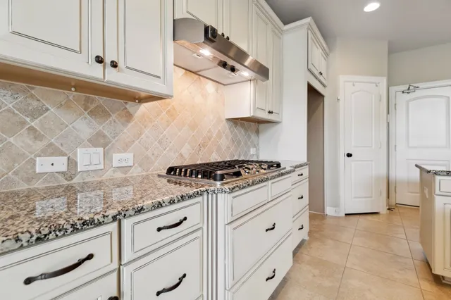 a white kitchen with granite countertop a stove and a sink