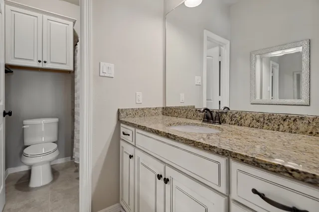 a bathroom with a granite countertop sink and a toilet