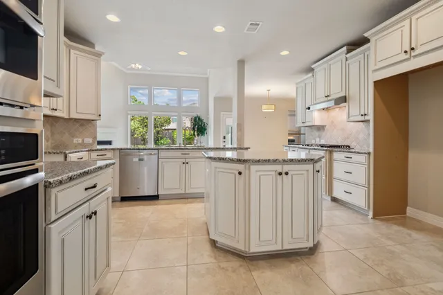 a kitchen with stainless steel appliances granite countertop a stove top oven a sink a refrigerator and white cabinets