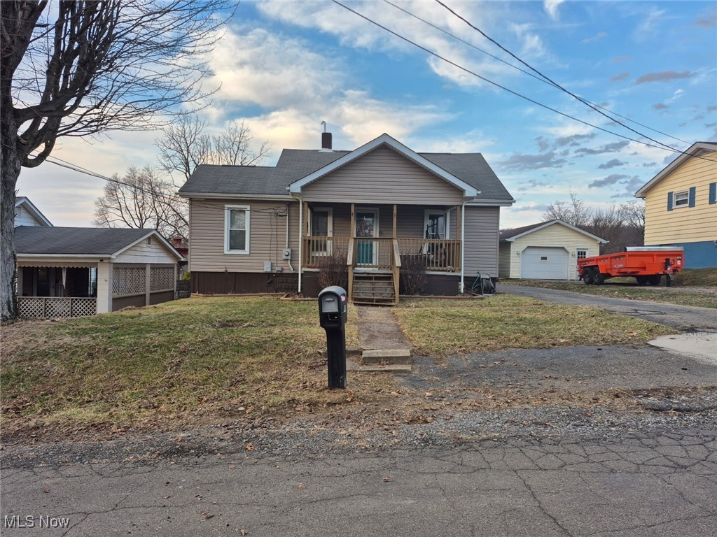 Bungalow featuring aphalt driveway, an outbuilding, covered porch, and a front lawn