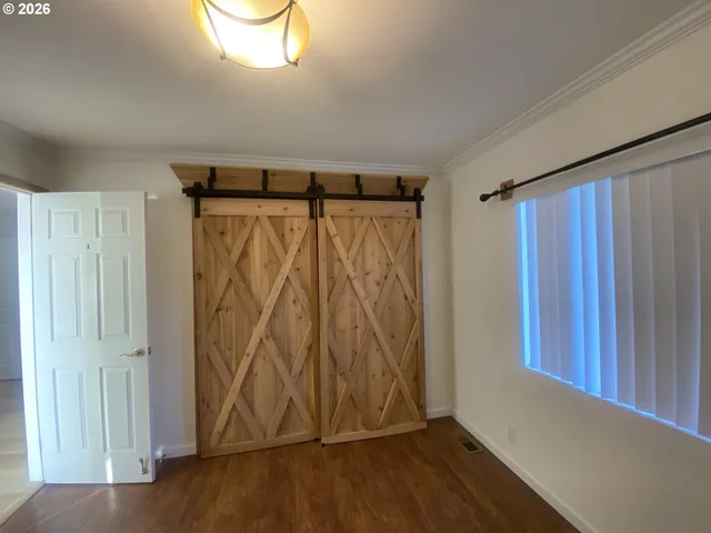 a view of an empty room with window and hardwood floor