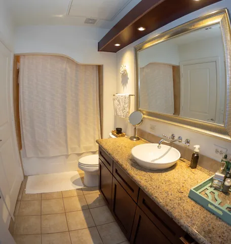 a bathroom with a granite countertop sink a toilet a mirror and shower