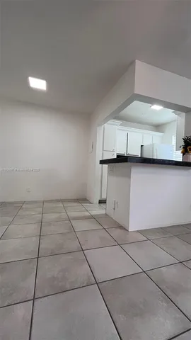 a view of an empty room with kitchen and cabinets
