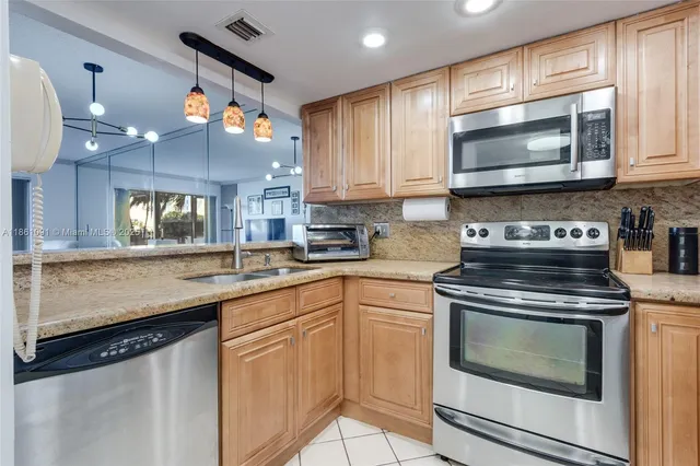 a kitchen with granite countertop a stove top oven a sink and dishwasher a refrigerator with wooden cabinets