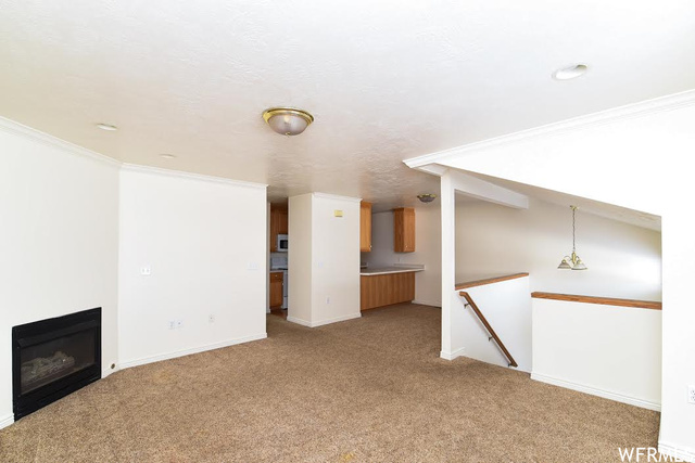 1130 North 200 West Bountiful, UT 84010 - Photo 3 of 11 Unfurnished living room featuring crown molding, a glass covered fireplace, and light carpet
