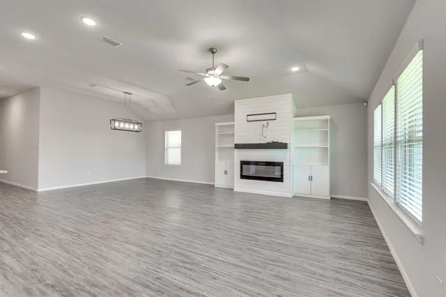 an empty room with windows fireplace and a kitchen view