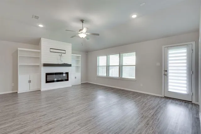 an empty room with wooden floor fireplace and windows