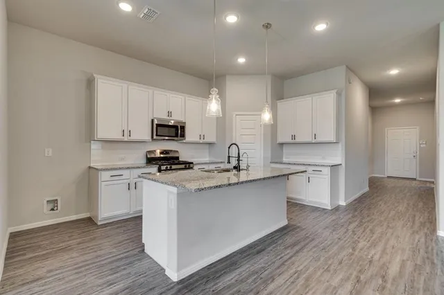 a kitchen with stainless steel appliances granite countertop a stove top oven a sink a refrigerator and white cabinets with wooden floor