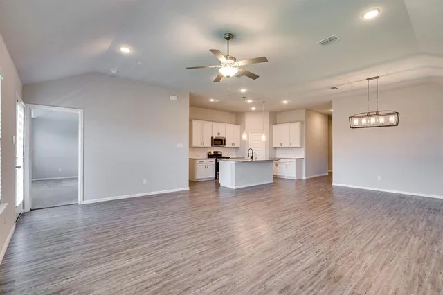 a view of an empty room with wooden floor and a kitchen