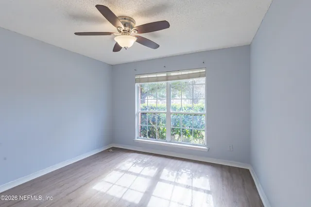 an empty room with wooden floor fan and windows