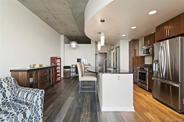 a kitchen with stainless steel appliances kitchen island granite countertop a refrigerator a stove a sink dishwasher and a dining table with wooden floor