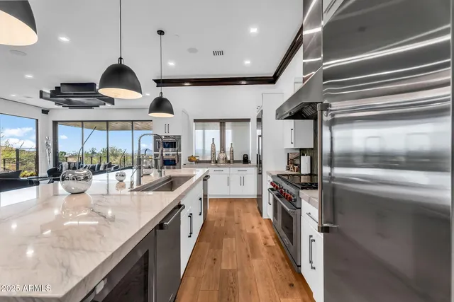 a kitchen with stainless steel appliances kitchen island granite countertop a dining table chairs sink and white cabinets