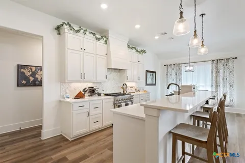 a kitchen with stainless steel appliances kitchen island granite countertop a stove top oven a sink a dining table and chairs with wooden floor
