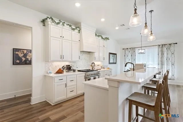a kitchen with stainless steel appliances kitchen island granite countertop a stove top oven a sink a dining table and chairs with wooden floor