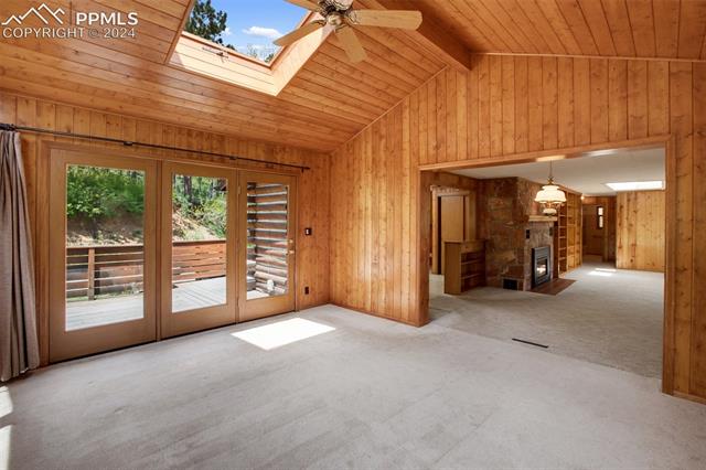 4980 Dodd Road Cascade, CO 80809 - Photo 21 of 48 Carpeted sunroom with a peak into the living room, ceiling fan, wooden ceiling, wooden walls, and vaulted ceiling with skylight