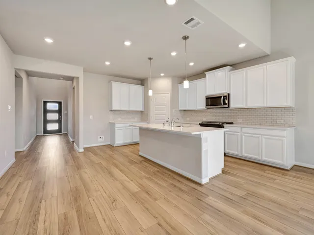 a large kitchen with kitchen island a sink dishwasher a stove a refrigerator and white cabinets with wooden floor