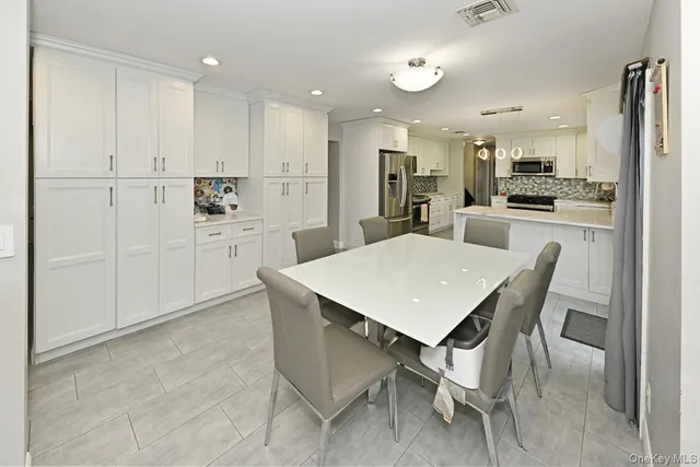 a kitchen with a dining table chairs refrigerator and white cabinets