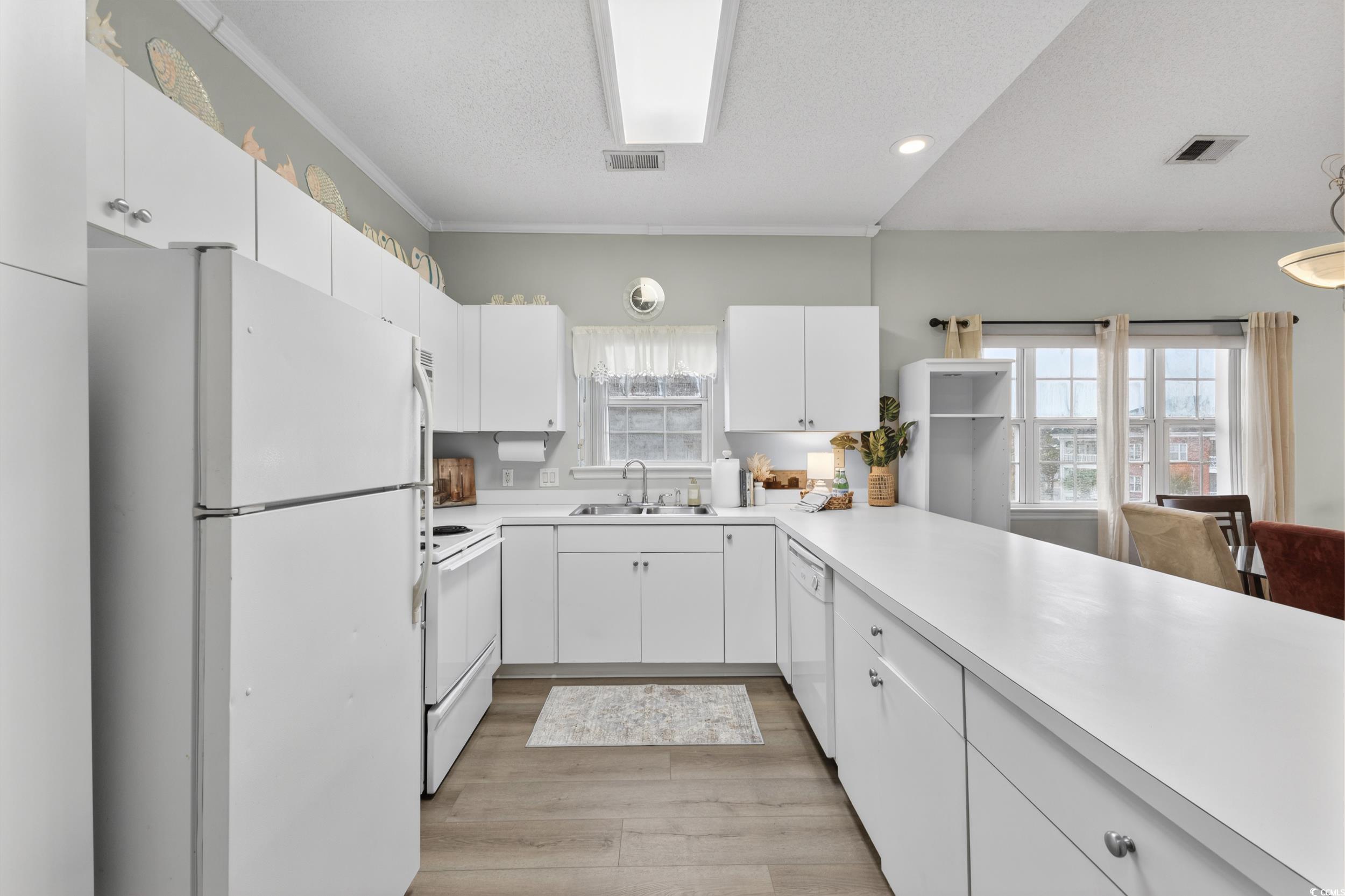 3915 Gladiola Court, Unit 301 Myrtle Beach, SC 29588 - Photo 4 of 24 Kitchen featuring white appliances, white cabinets, light countertops, light wood finished floors, and plenty of natural light