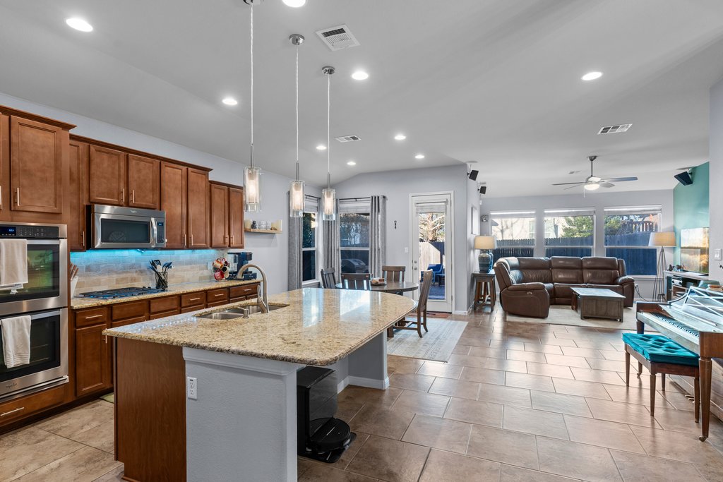 2902 Tempe Drive Cedar Park, TX 78641 - Photo 7 of 38 Kitchen featuring a ceiling fan, stainless steel appliances, a center island with sink, light stone countertops, and backsplash