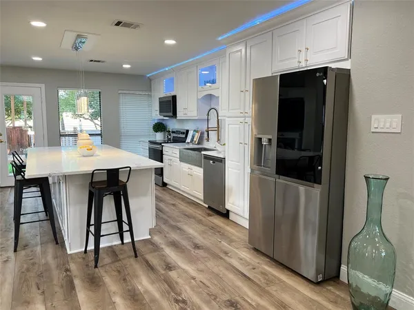 a kitchen with stainless steel appliances kitchen island granite countertop a refrigerator a stove top oven a sink dishwasher and white cabinets with wooden floor