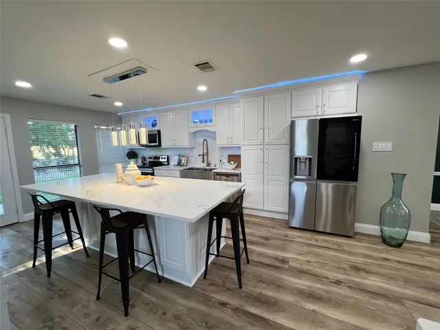 a kitchen with stainless steel appliances a dining table chairs refrigerator and microwave