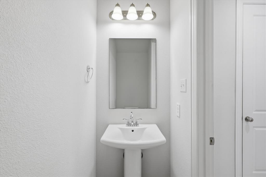 519 Sequoia Street Allen, TX 75002 - Photo 16 of 38 Pedestal sink with chrome faucet, complemented by a rectangular wall mirror and a three-light vanity fixture