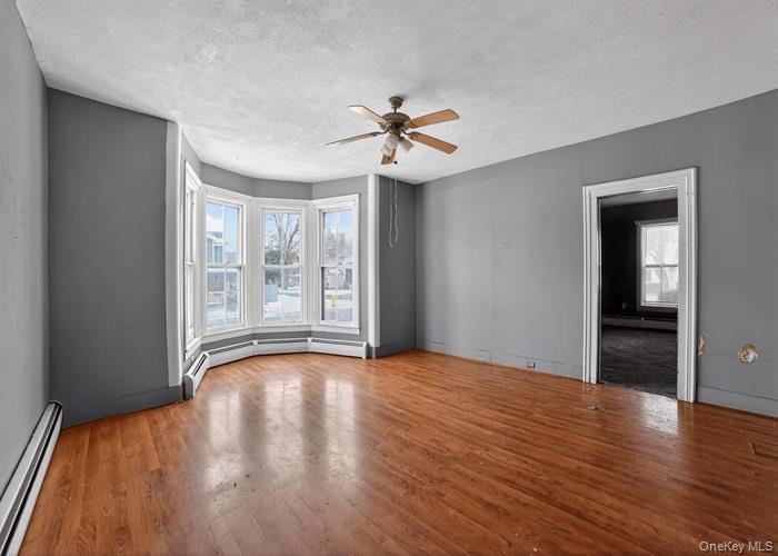 62 George Street Owego, NY 13827 - Photo 6 of 21 Spare room with a baseboard heating unit, a textured ceiling, plenty of natural light, ceiling fan, and light wood-style floors