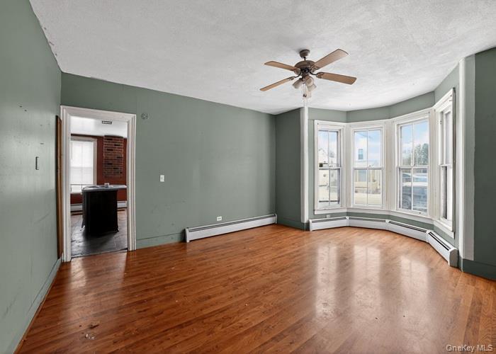 62 George Street Owego, NY 13827 - Photo 7 of 21 Unfurnished room with a textured ceiling, baseboard heating, wood finished floors, and a ceiling fan