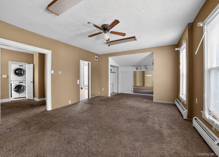 62 George Street Owego, NY 13827 - Photo 8 of 21 Unfurnished living room featuring a baseboard heating unit, stacked washer and clothes dryer, carpet, a textured ceiling, and a ceiling fan