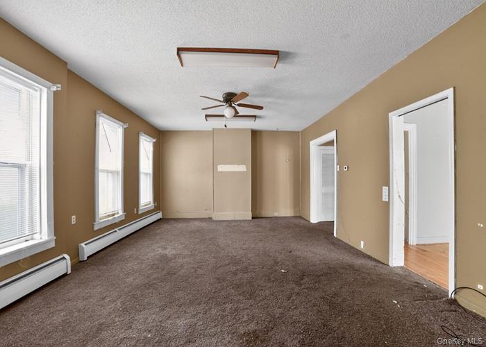 62 George Street Owego, NY 13827 - Photo 9 of 21 Carpeted spare room with a baseboard heating unit, a textured ceiling, and a ceiling fan