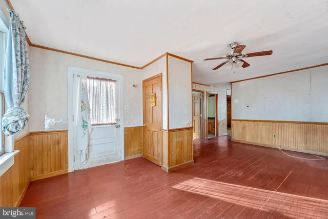 a view of an empty room with wooden floor and a ceiling fan