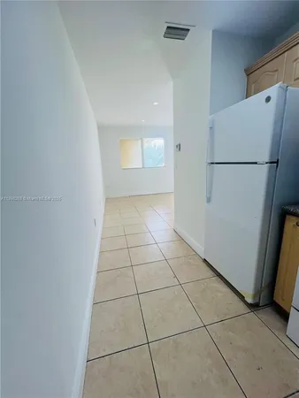 a view of a refrigerator in kitchen and an empty room in wooden floor