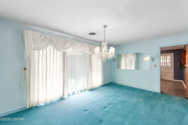 an empty room with chandelier fan and kitchen view