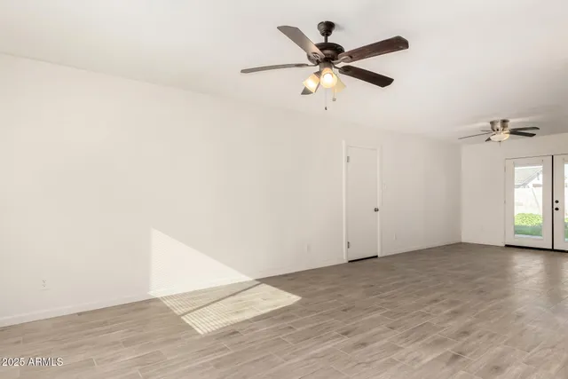 an empty room with wooden floor ceiling fan and windows