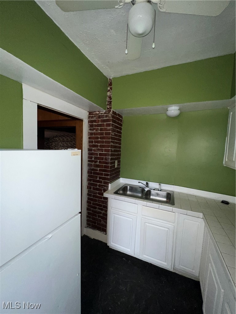 1334 Penhurst Road Cleveland, OH 44110 - Photo 15 of 20 Kitchen featuring tile counters, white cabinets, brick wall, refrigerator, and a sink