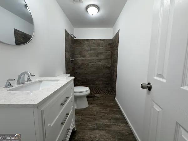 a bathroom with a granite countertop sink a toilet a mirror and shower