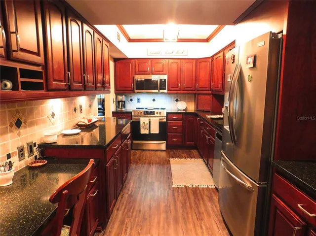 a kitchen with stainless steel appliances granite countertop a refrigerator a sink dishwasher a stove and white countertops with wooden floor