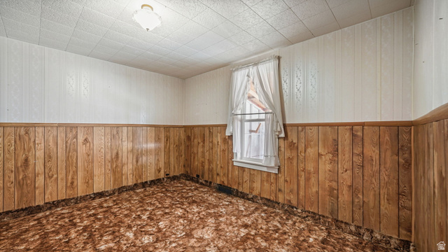 44 Shriver Street Eureka, UT 84628 - Photo 9 of 43 Room featuring wood-finish paneling, patterned wall covering, a grid-pattern ceiling, a single-hung window, and an overhead light fixture