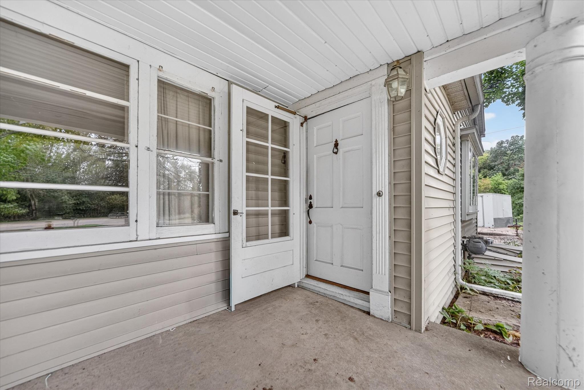 1730 Haslett Road Haslett, MI 48840 - Photo 6 of 31 Covered front porch with concrete flooring, multiple windows, a paneled entry door, and exterior siding