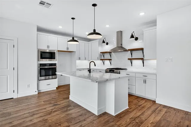 a kitchen with stainless steel appliances granite countertop a sink stove oven and white cabinets with wooden floor
